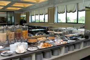 A buffet area with various food items, including pastries and cereals, arranged on a counter with a view of the outdoors through large windows. - Grand Hotel Duca di Mantova (Sesto San Giovanni)