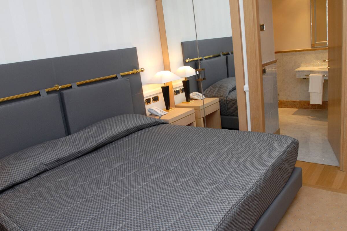 Una habitación de hotel moderna con una cama grande, mesitas de noche, un espejo y un baño visible a través de una puerta abierta.