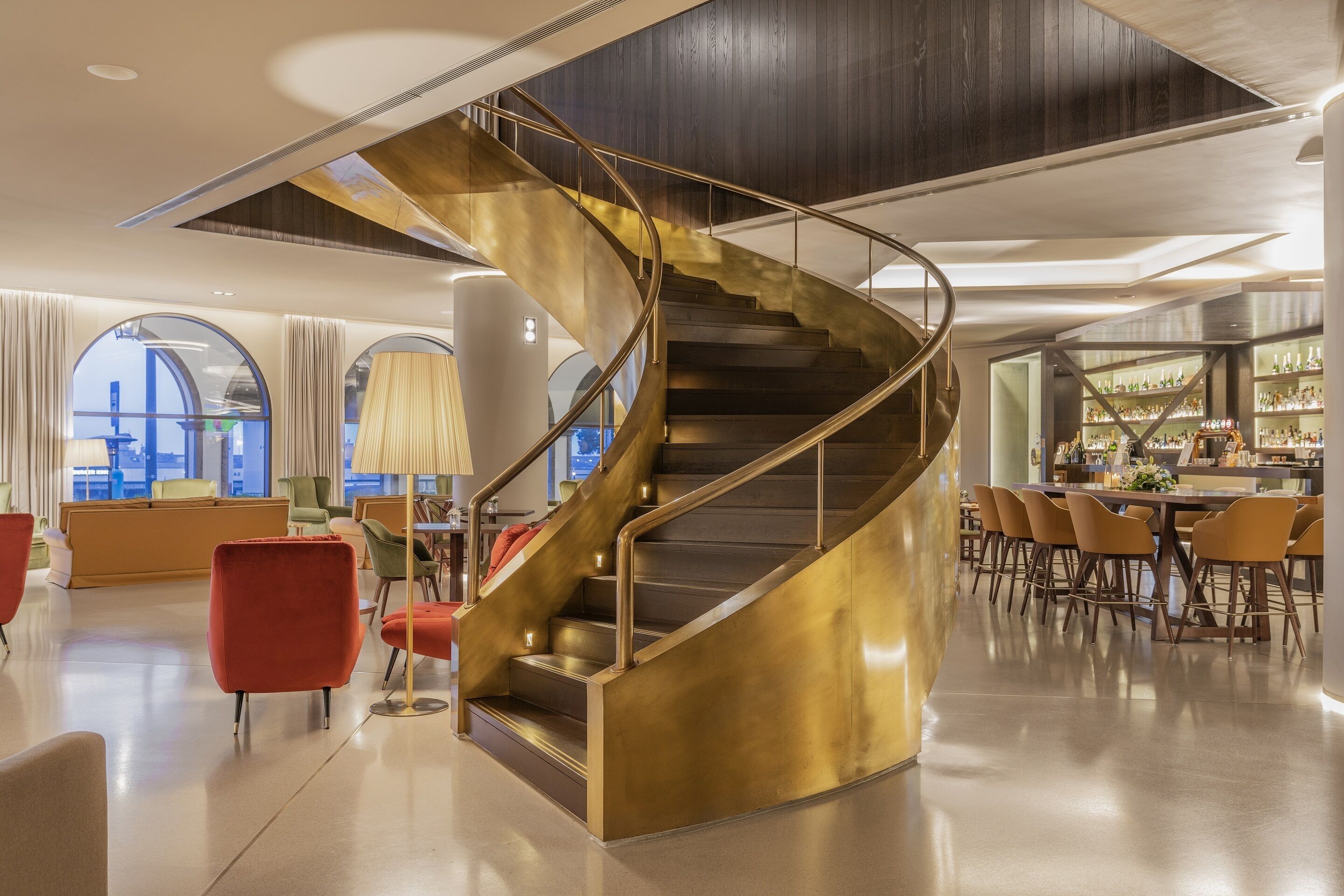 A modern interior with a spiral staircase, a bar area, and seating arrangements.