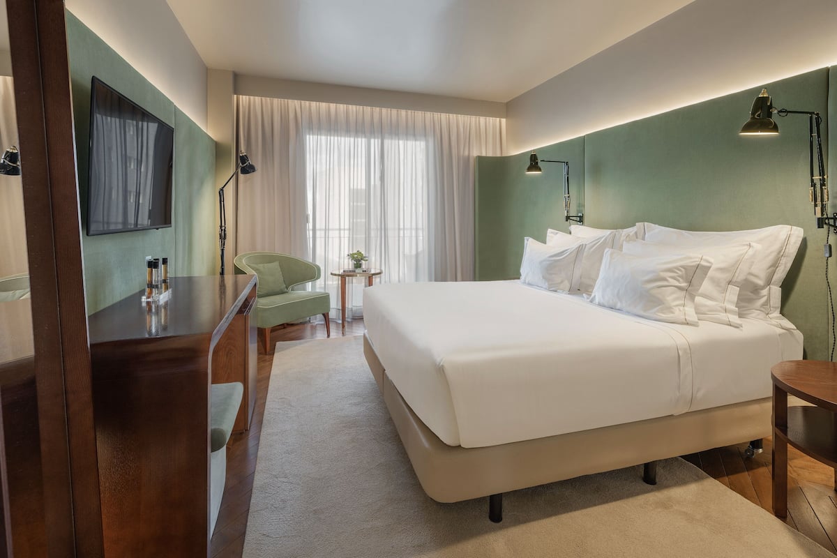 Een hotelkamer met een groot bed, een bureau, een stoel, een kleine tafel met een plant en een televisie aan de muur.
