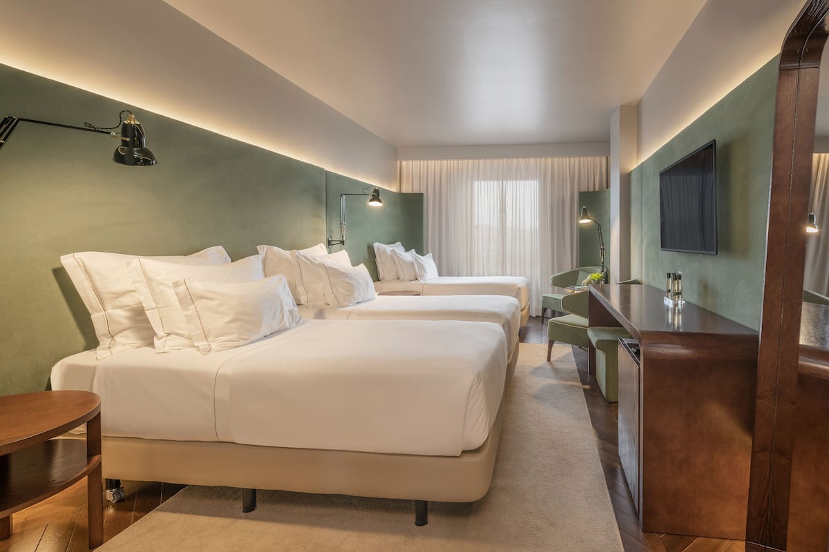 Een hotelkamer met twee bedden, een bureau, een stoel en een televisie aan de muur.