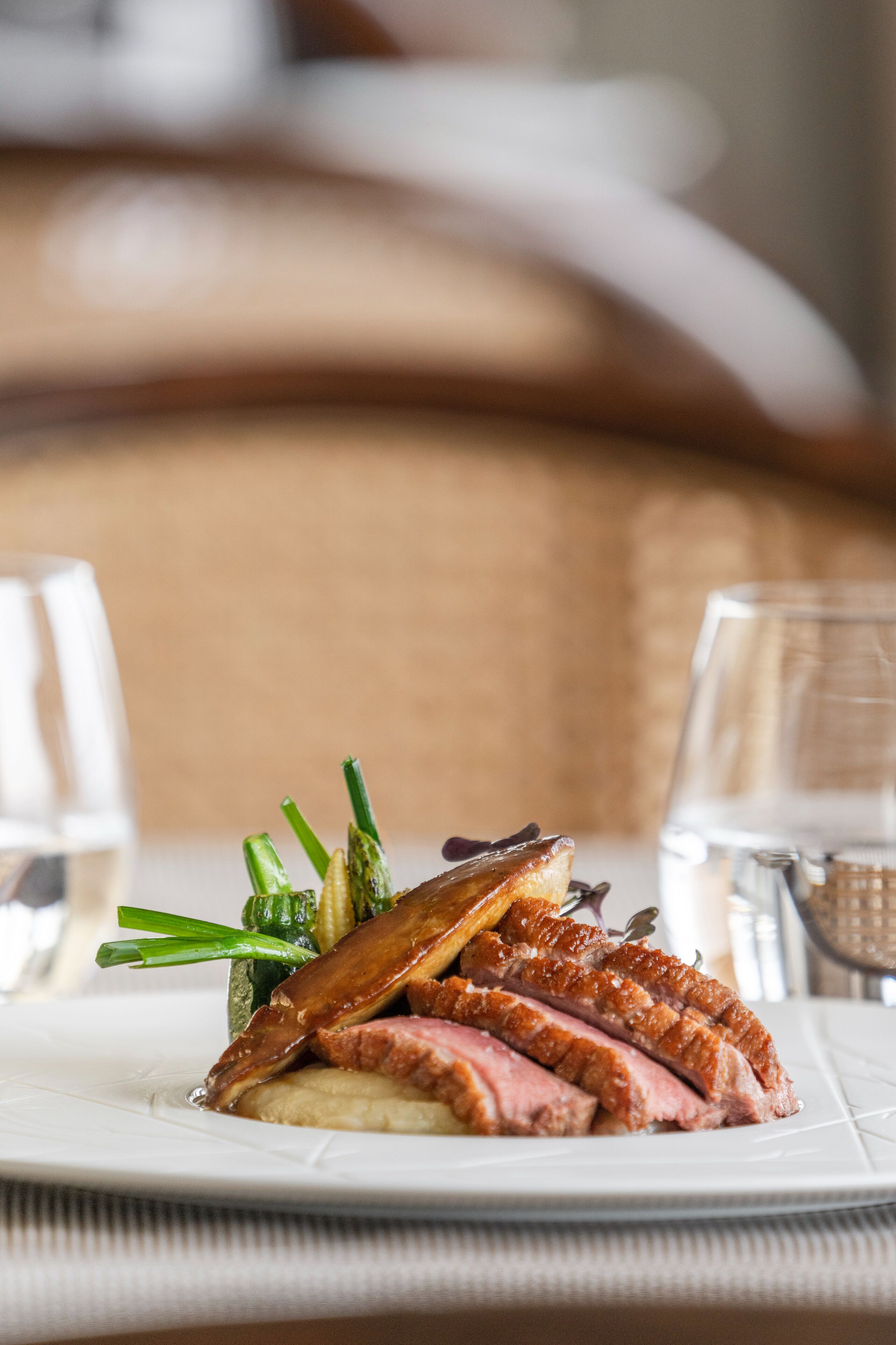 A plate of duck with vegetables on a white tablecloth.