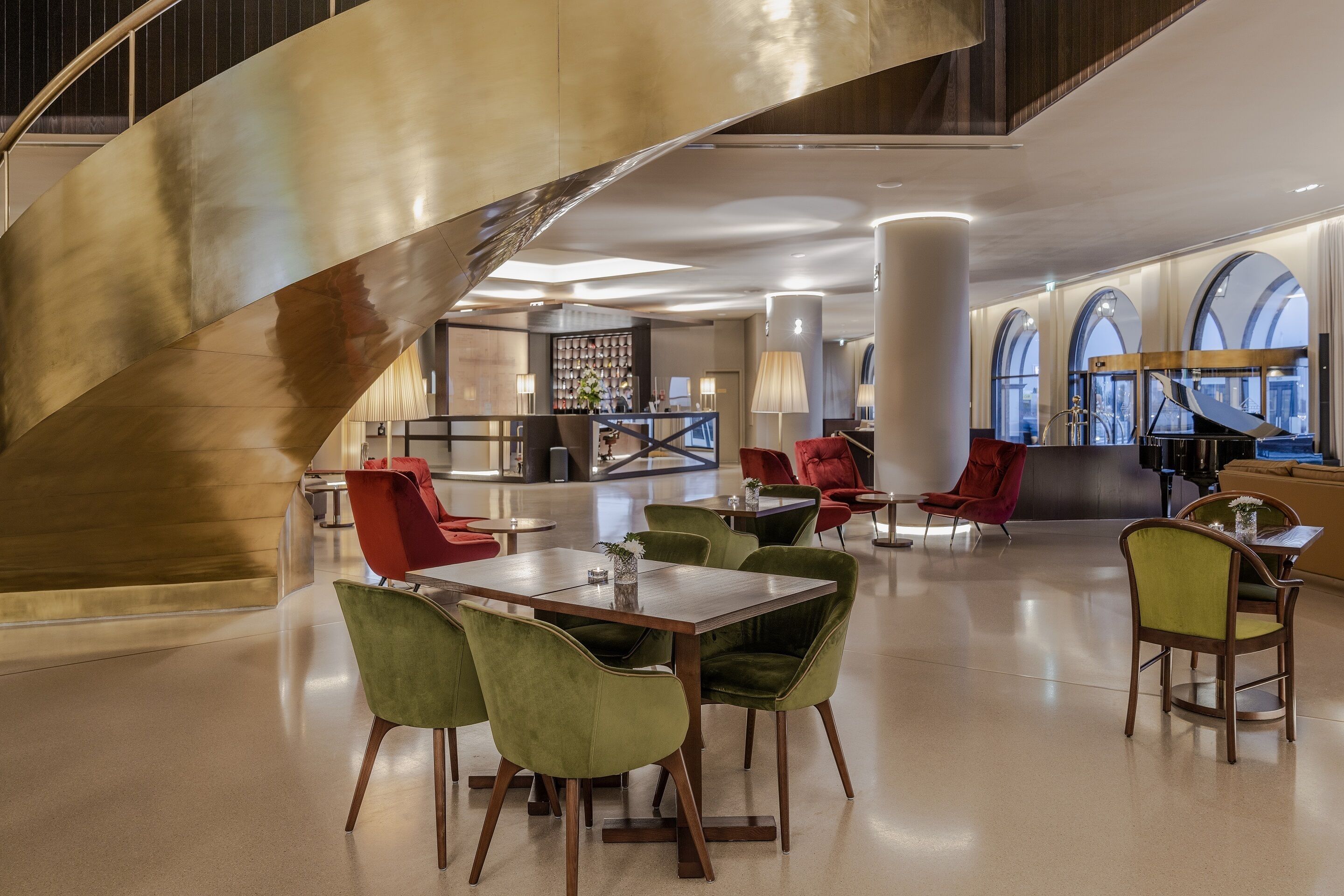 A spacious lobby with a central staircase, seating areas, and large windows.
