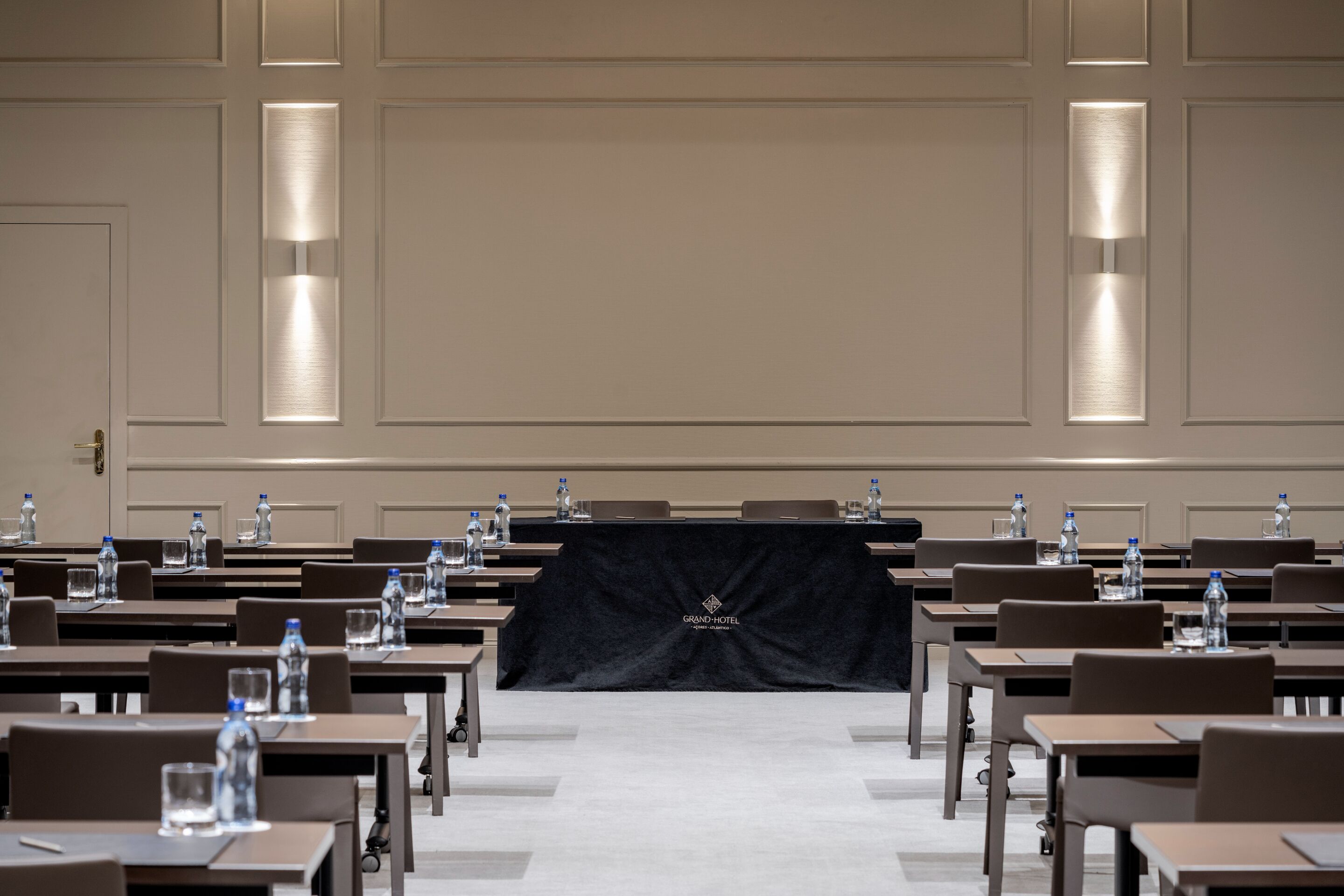 A conference room with rows of tables, water bottles, and glasses on each table.