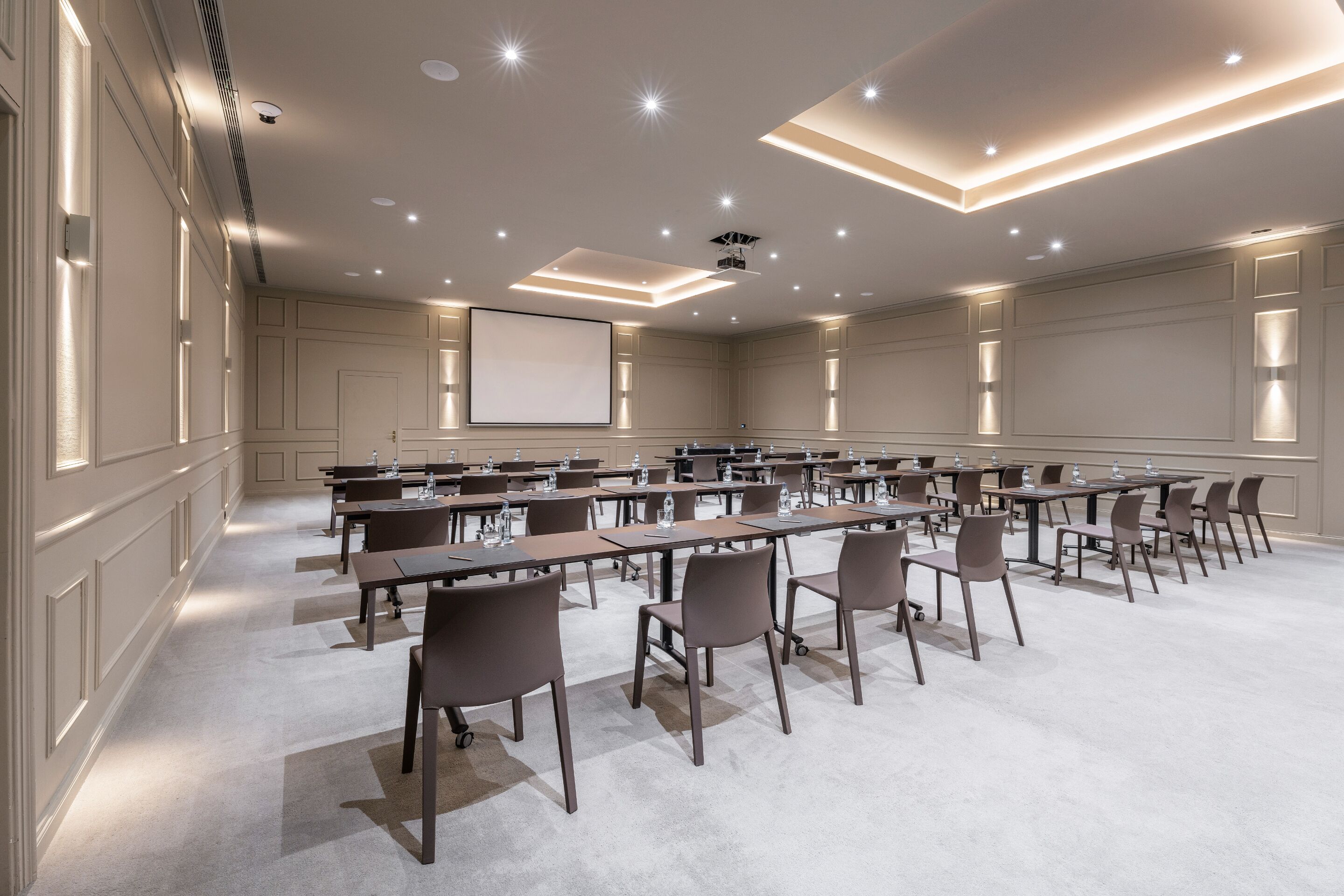 A conference room with multiple tables and chairs, a projector screen, and recessed lighting.