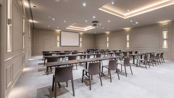 A conference room with multiple tables and chairs, a projector screen, and recessed lighting.