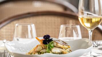 A dining table with a white plate of food, a glass of white wine, and a fork.
