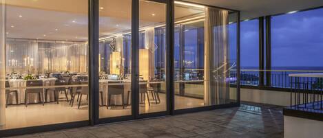 A modern dining area with a glass wall overlooking the sea.