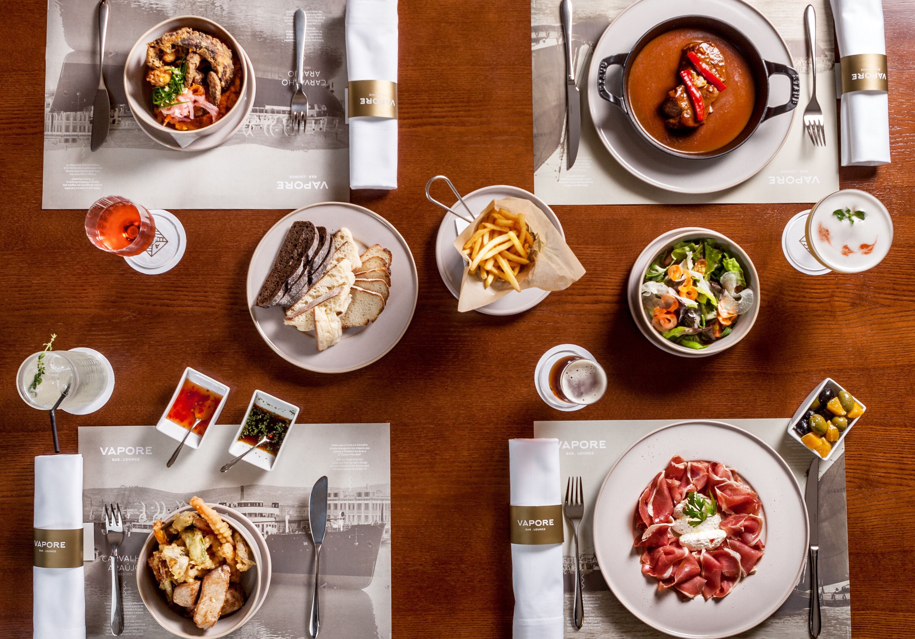 A dining table with various dishes, including a bowl of soup, a plate of meat, and a bowl of salad, along with cutlery and napkins.