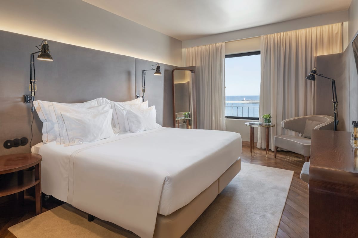 Een moderne hotelkamer met een groot bed, twee nachtkastjes, een bureau, een stoel en uitzicht op zee.