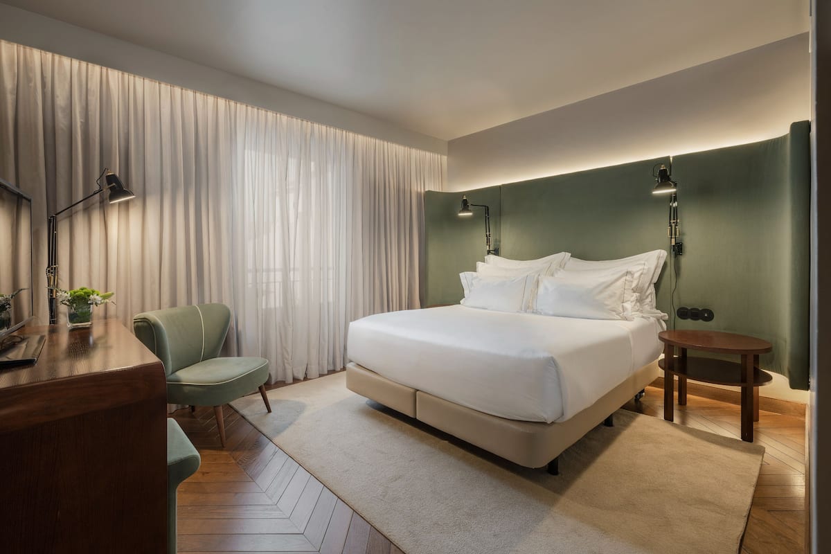 Een moderne hotelkamer met een groot bed, een bureau, een stoel en een bijzettafeltje.