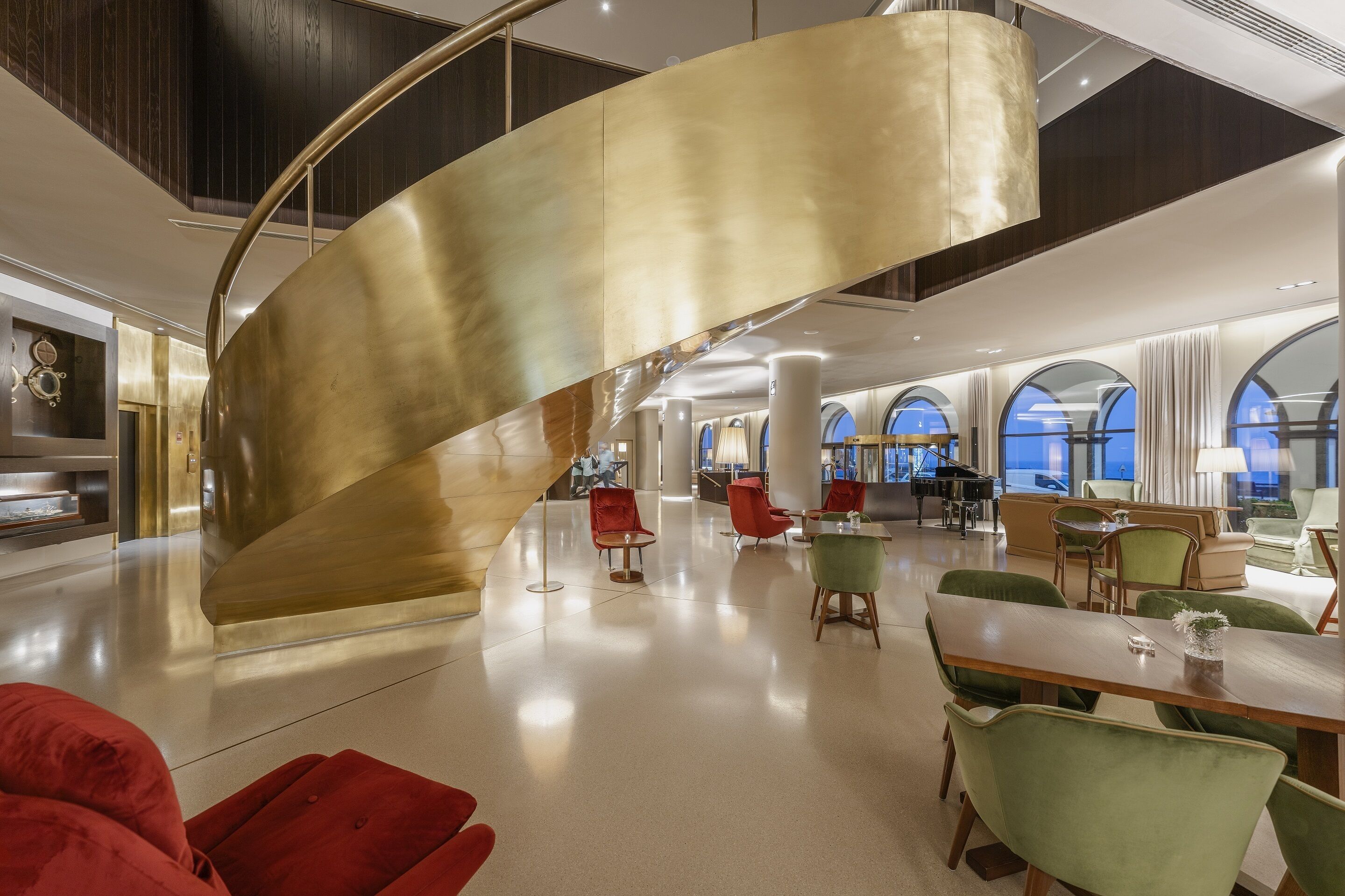 A spacious lobby with a curved golden staircase, modern furniture, and large windows offering views.