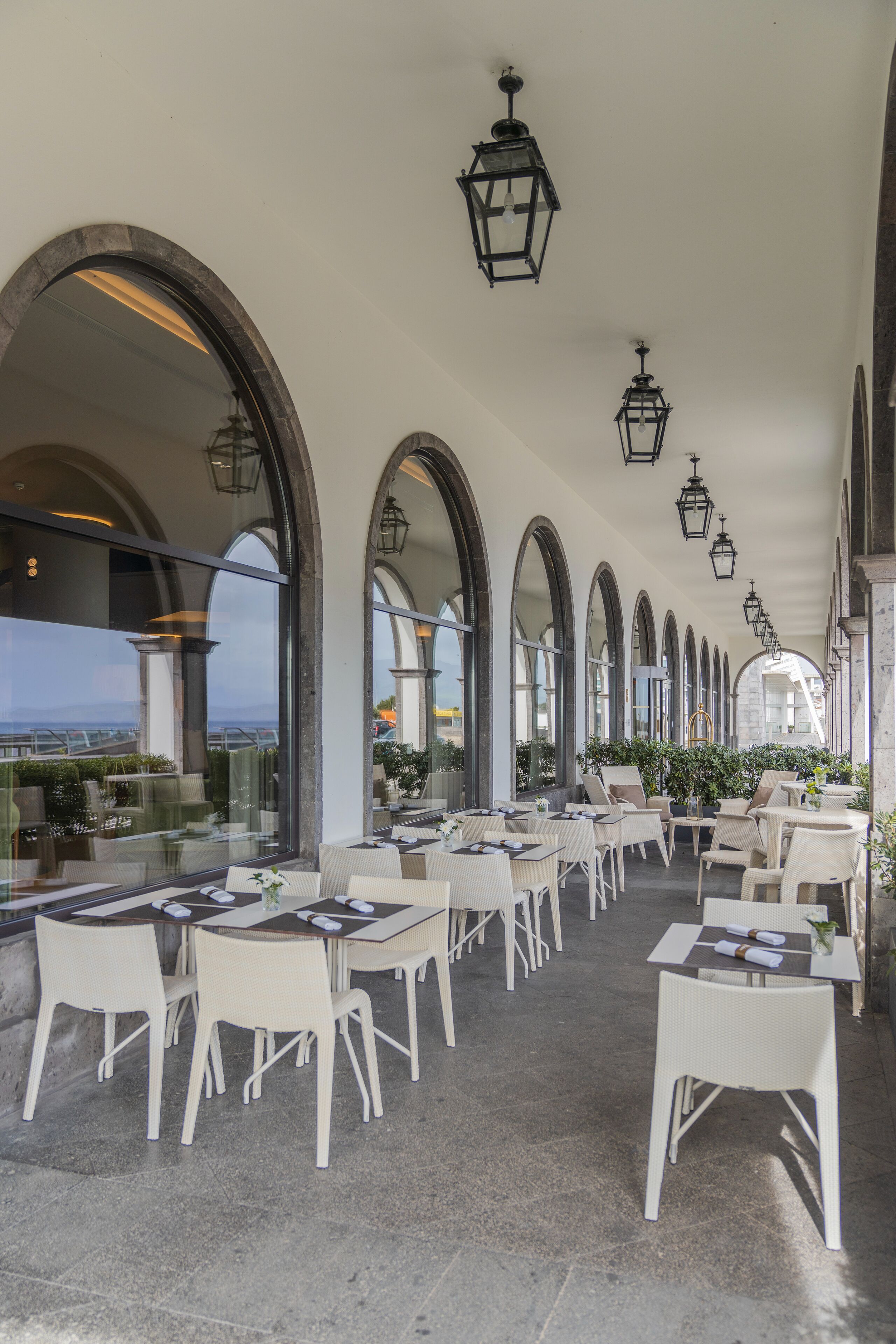 An outdoor dining area with white chairs and tables, arched ceilings, and hanging lanterns.