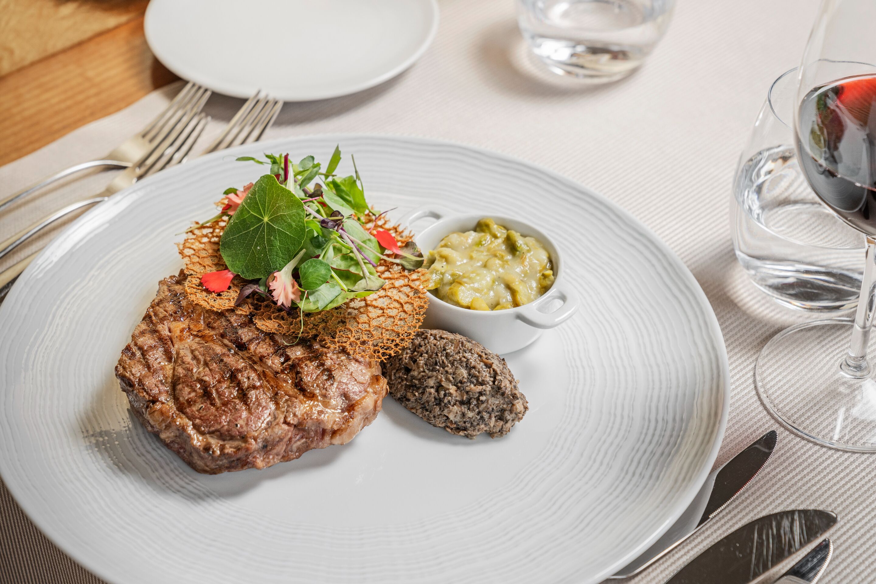 Un plato con un bistec, vegetales verdes y un tazón pequeño de salsa.