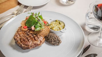 A plate with a steak, greens, and a small bowl of sauce.