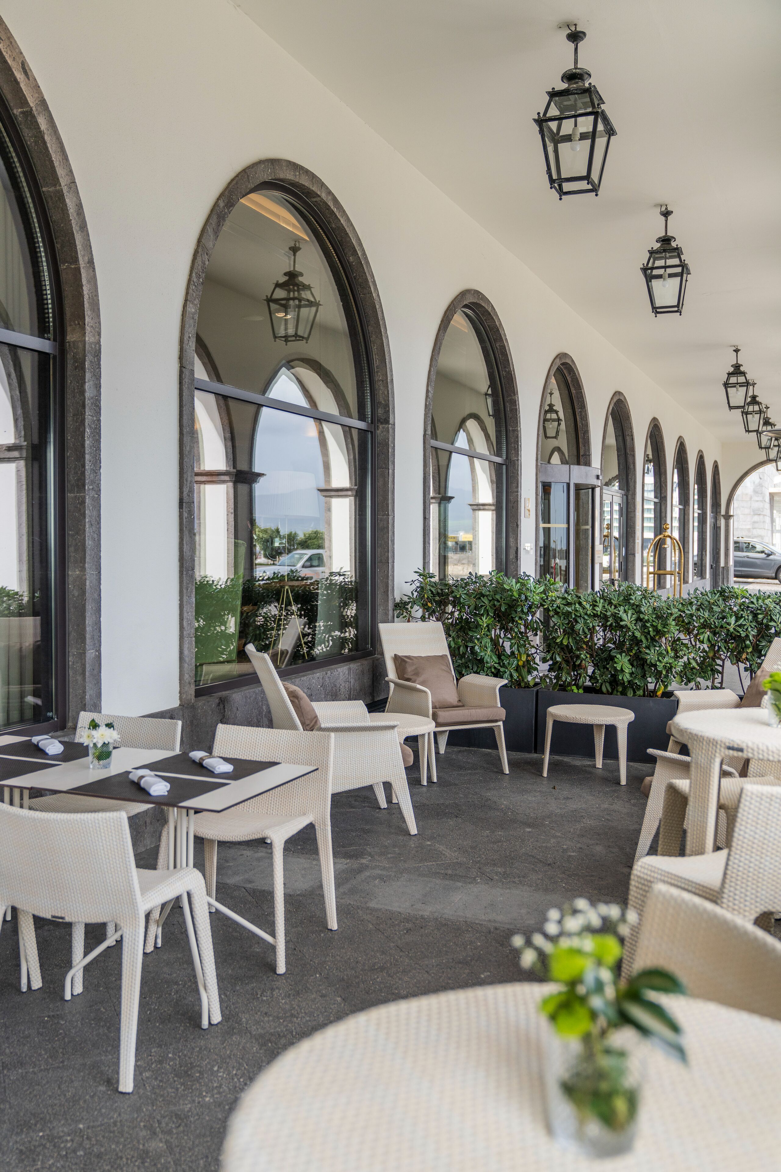 An outdoor seating area with white wicker furniture, arched windows, and hanging lanterns.
