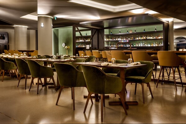 A restaurant with green velvet chairs, wooden tables, and a bar area with shelves of bottles. - Grand Hotel Açores Atlântico (Ponta Delgada)