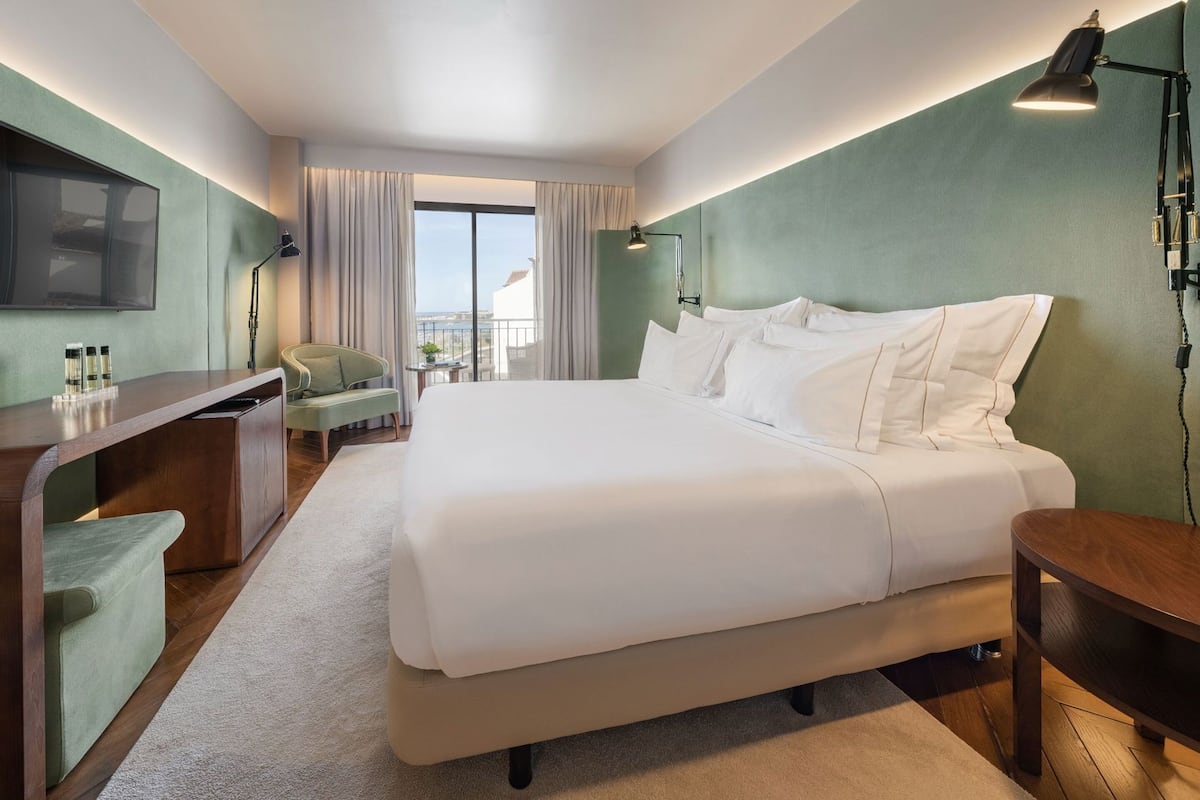 Een hotelkamer met een groot bed, een bureau, een stoel en een balkon met gordijnen.