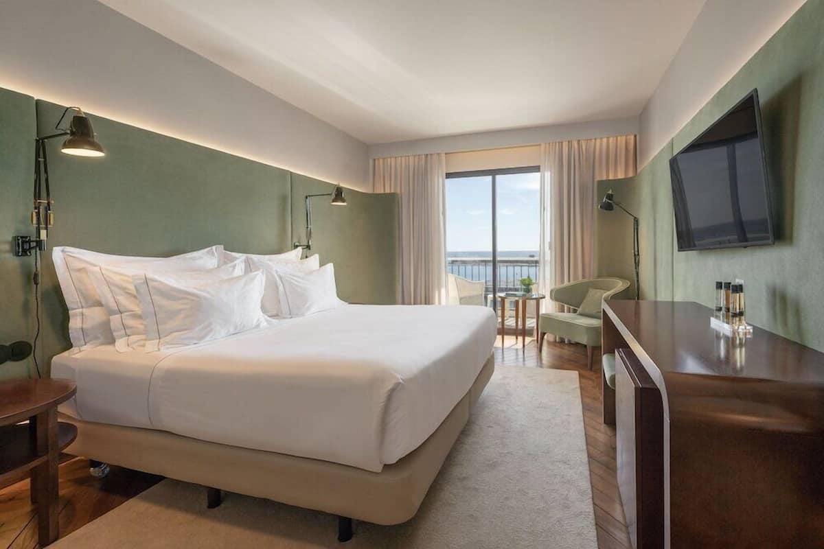 Een hotelkamer met een groot bed, een bureau, een stoel, een televisie en uitzicht op zee.