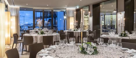 A dining area with round tables set for a formal meal, featuring white tablecloths and silverware.