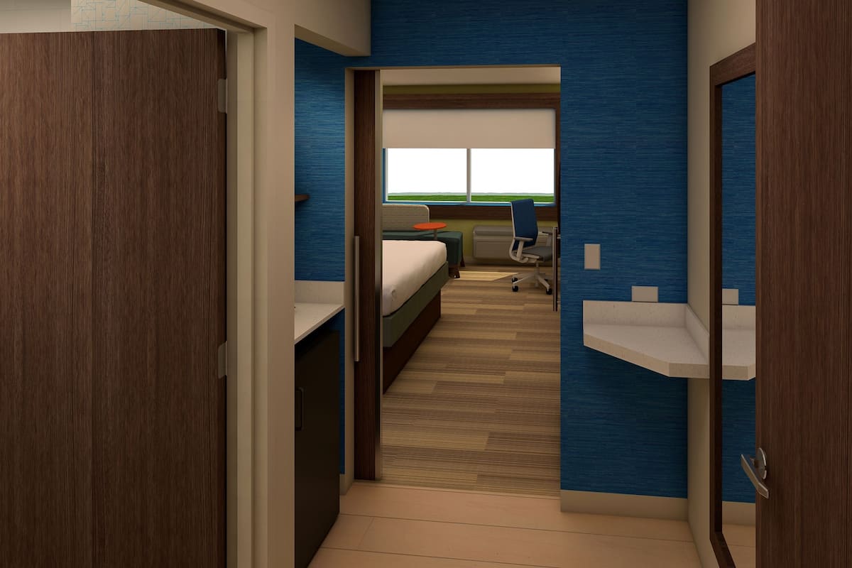A hotel room with a bed, a desk, a chair, and a window with a view of a green field.