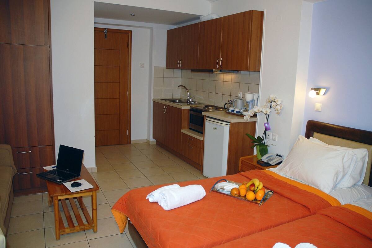 Una habitación de hotel con cama, un escritorio pequeño con una computadora portátil, una cocina y un baño.