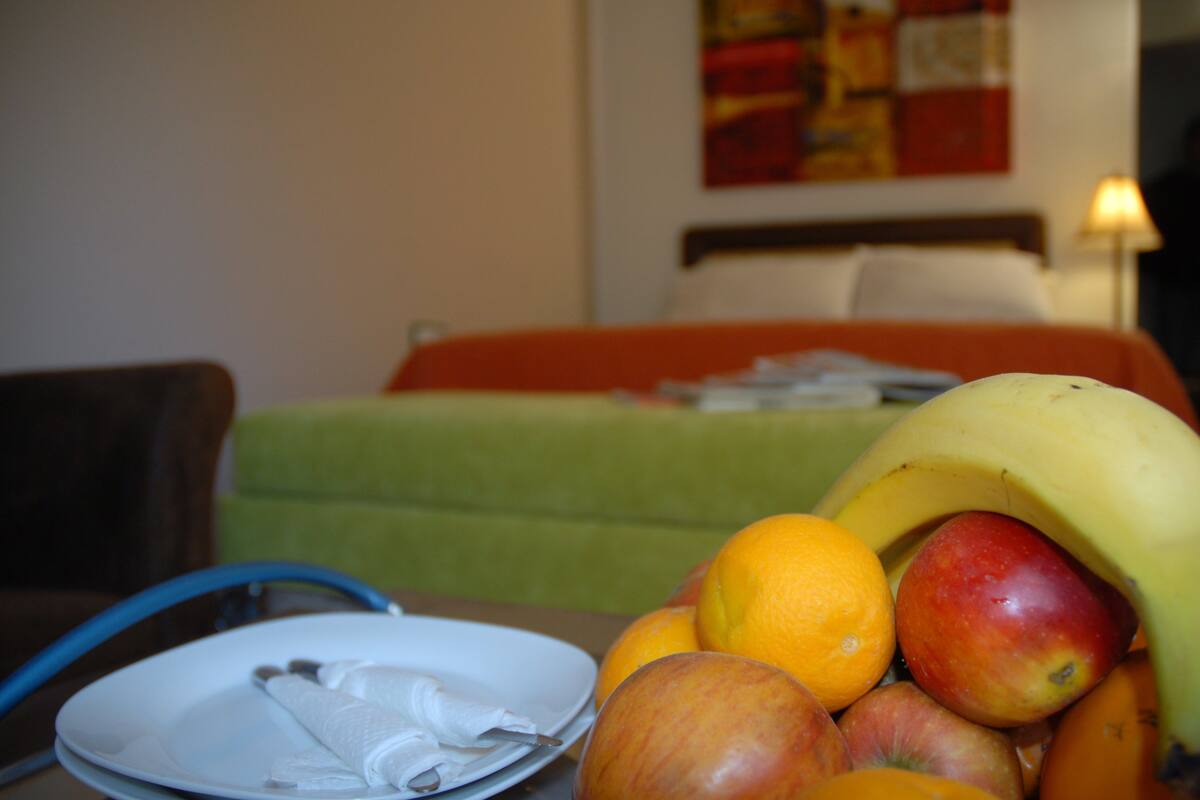Una mesa de comedor con frutas, un plato con un tenedor y una silla.