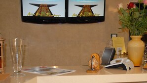 A reception desk with two monitors displaying 'Active Graphics Technology', a vase with flowers, a globe, a phone, and a magazine. - Hotel Aria (Samos)