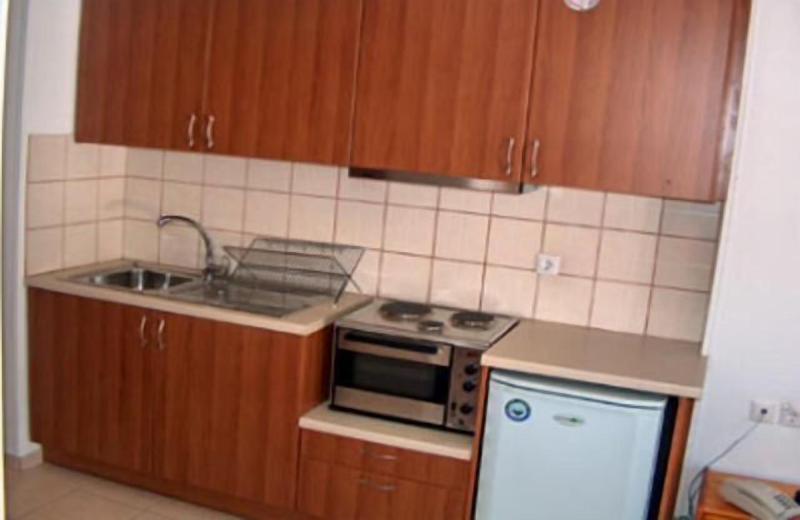 Una cocina compacta con armarios de madera, un lavamanos, horno empotrado y un refrigerador pequeño.