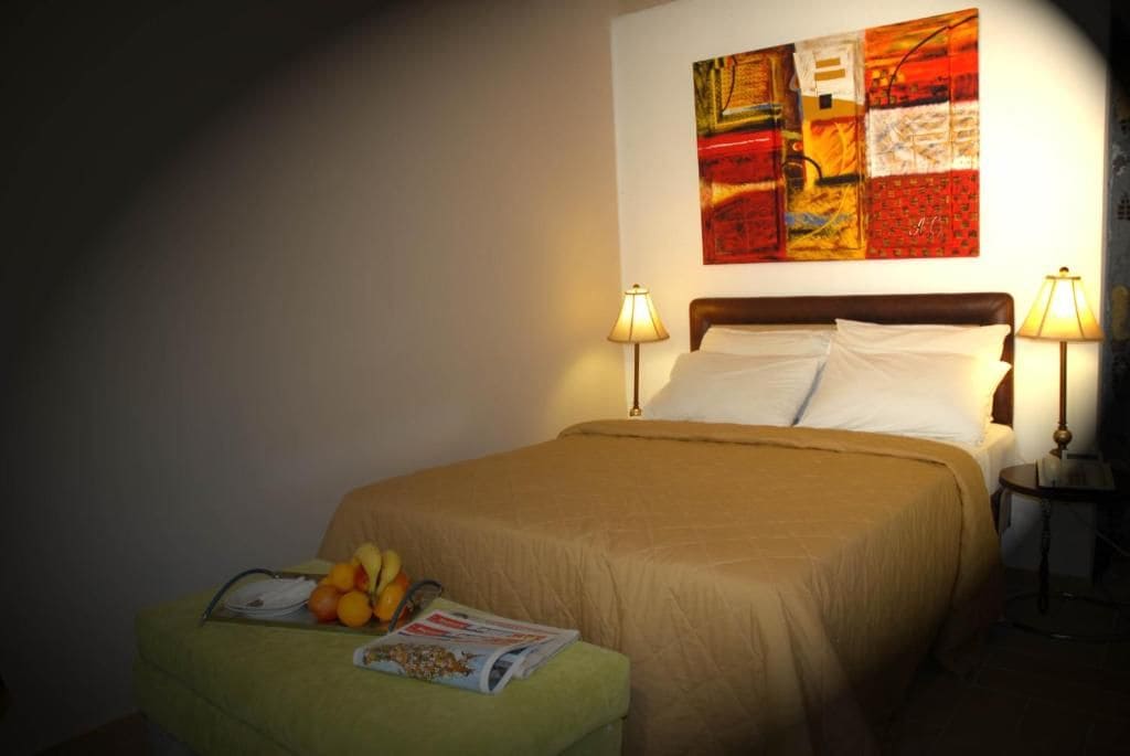 A hotel room with a bed, two bedside lamps, a fruit basket, and a magazine on the nightstand.