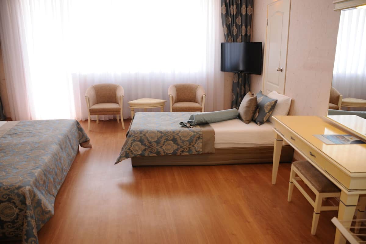 Une chambre d’hôtel comprenant un lit, deux fauteuils, une petite table, un bureau, une télévision et une fenêtre avec des rideaux.