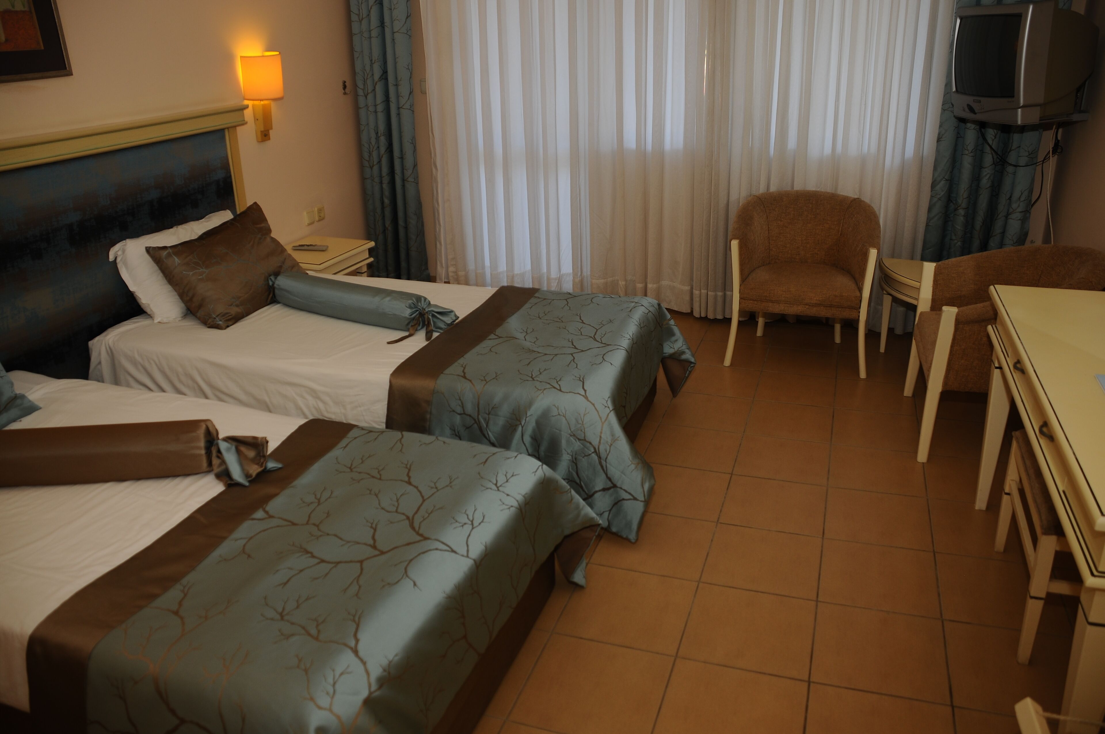 Quarto de hotel com duas camas, televisão, uma cadeira e uma mesa.