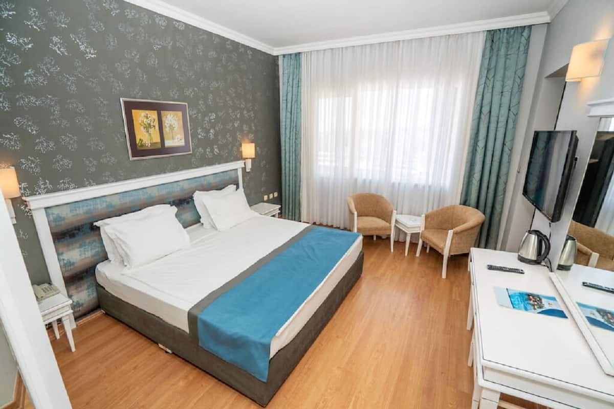 A hotel room with a bed, a desk, a chair, a TV, and a window with curtains.