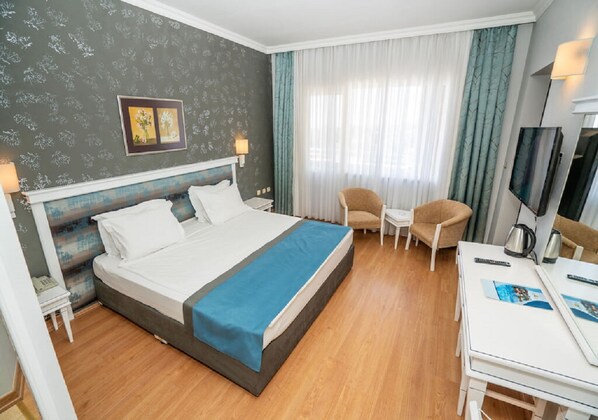 A hotel room with a bed, a desk, a chair, a TV, and a window with curtains.