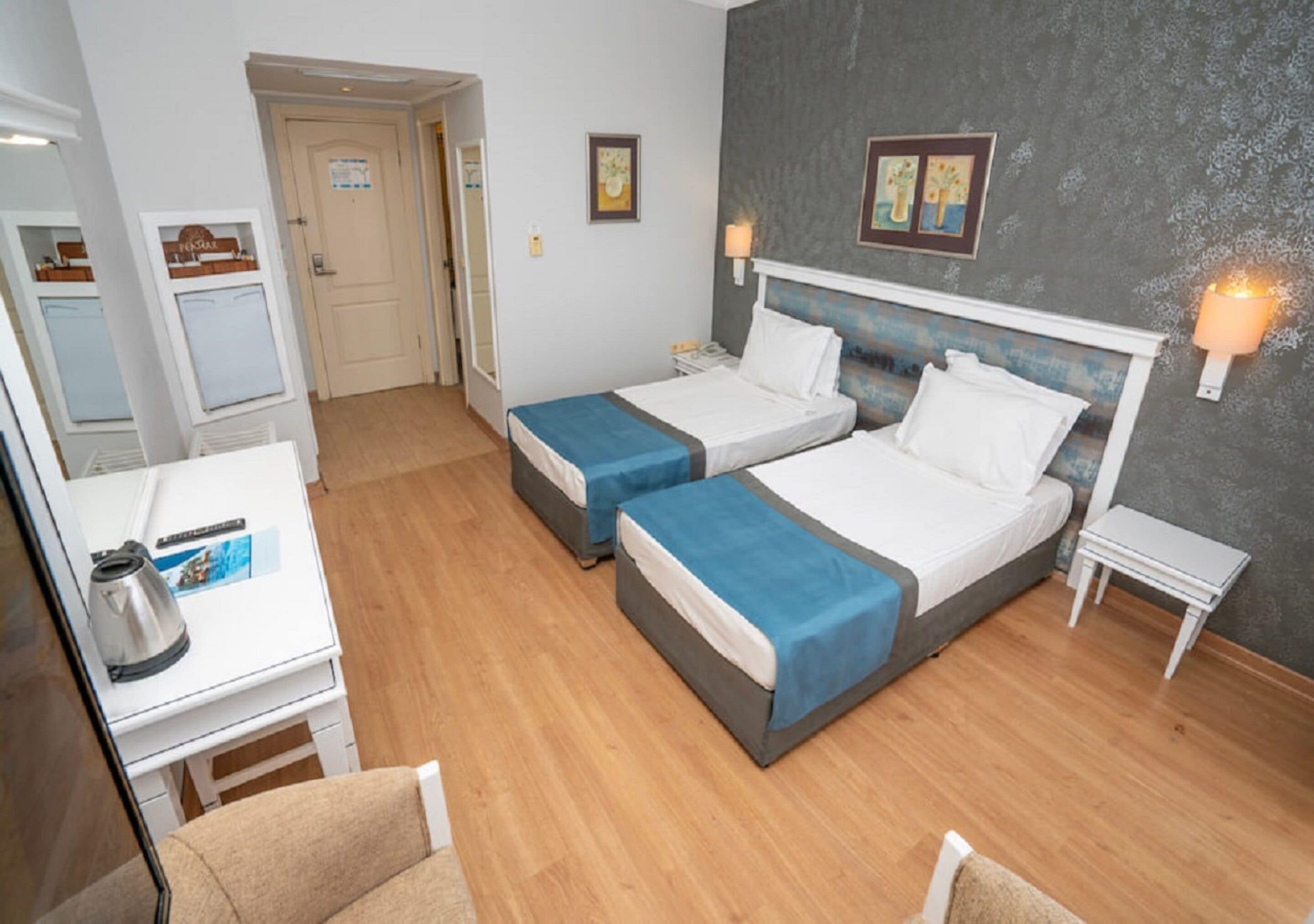 A hotel room with two beds, a desk, a chair, and a small table.
