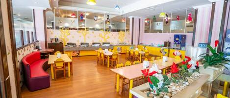 Um restaurante infantil com mesas e cadeiras de madeira, área de recreação e balcão com alimentos.