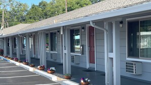 Un motel con una hilera de habitaciones, cada una con ventana y puerta. Hay plantas en macetas a lo largo del pasillo.