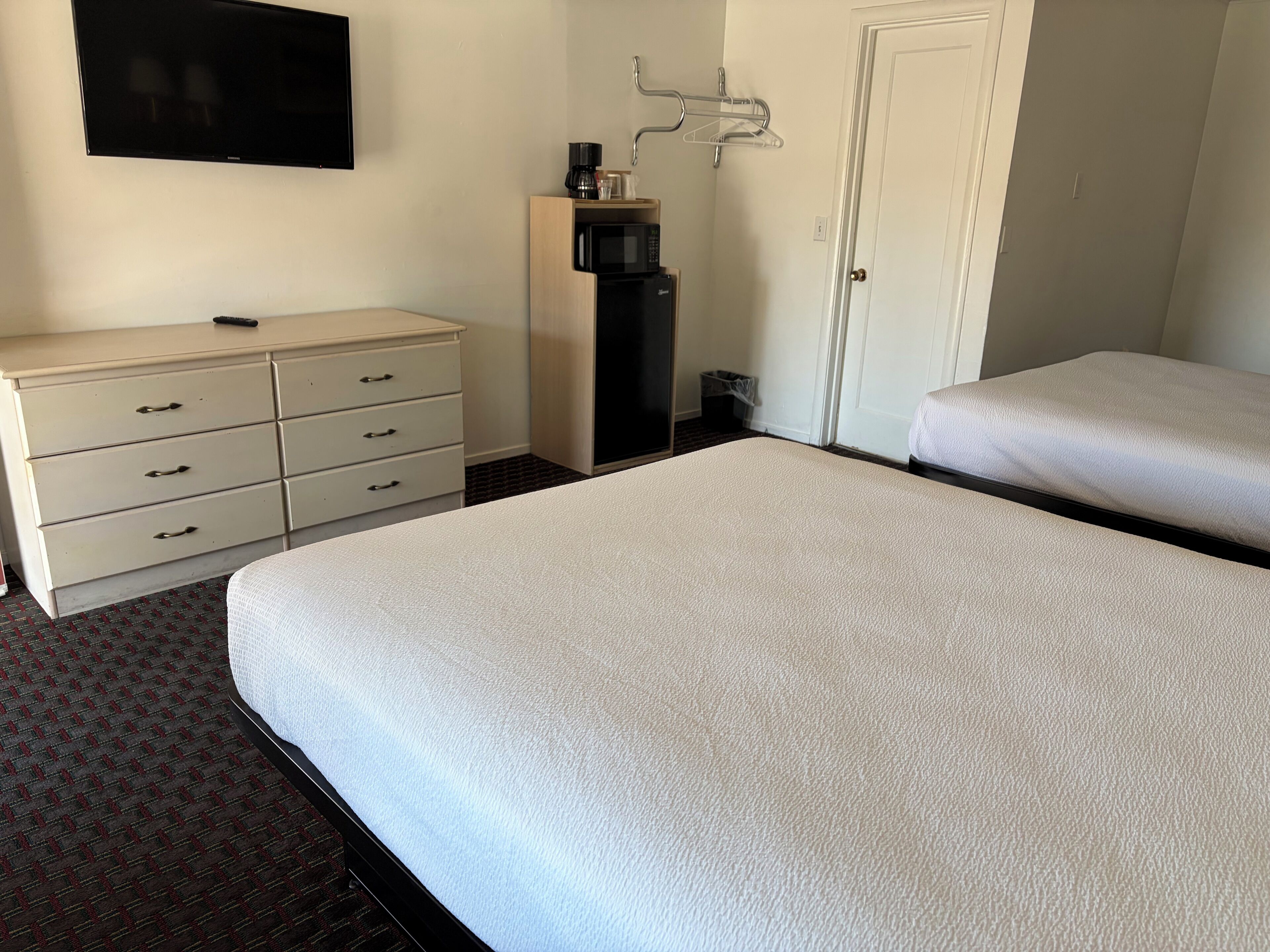 A hotel room with a bed, a dresser, a TV, a microwave, and a door.
