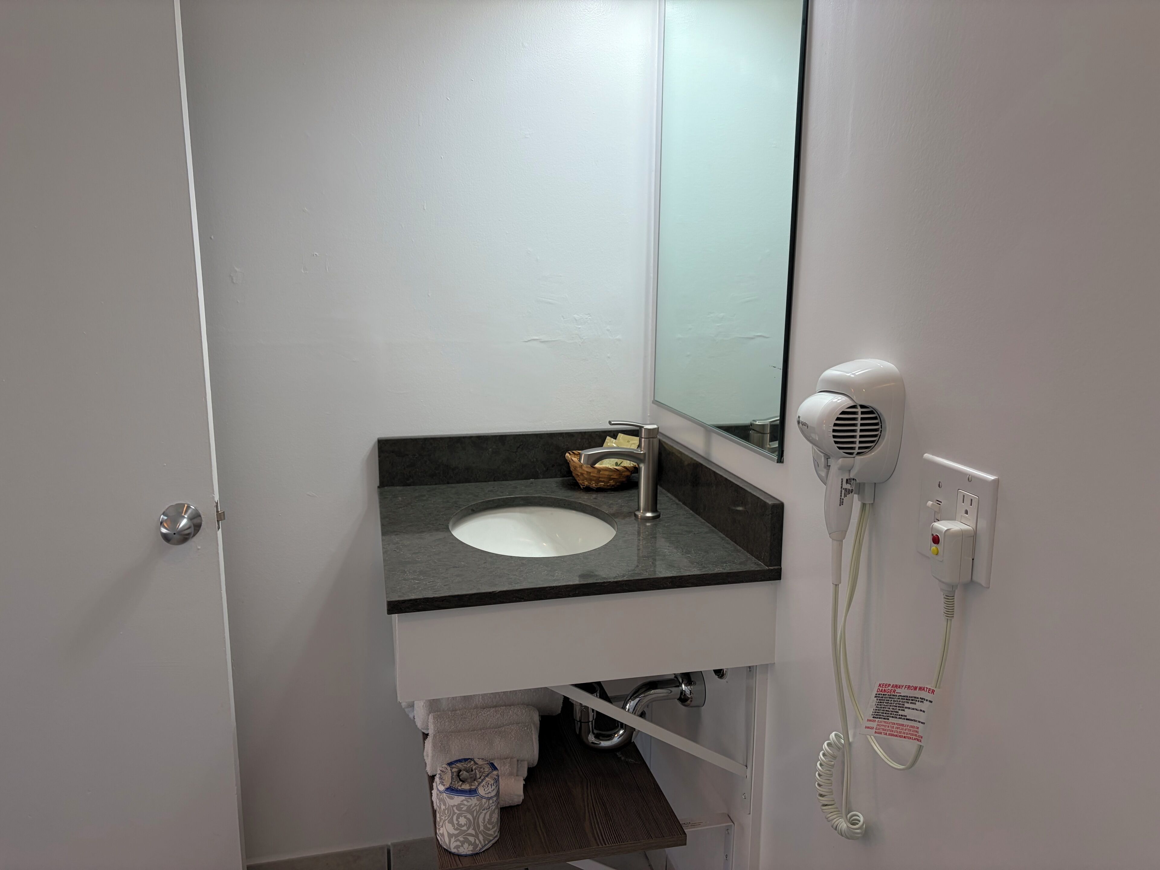 A bathroom with a white sink, a mirror, a hairdryer, and a towel rack.