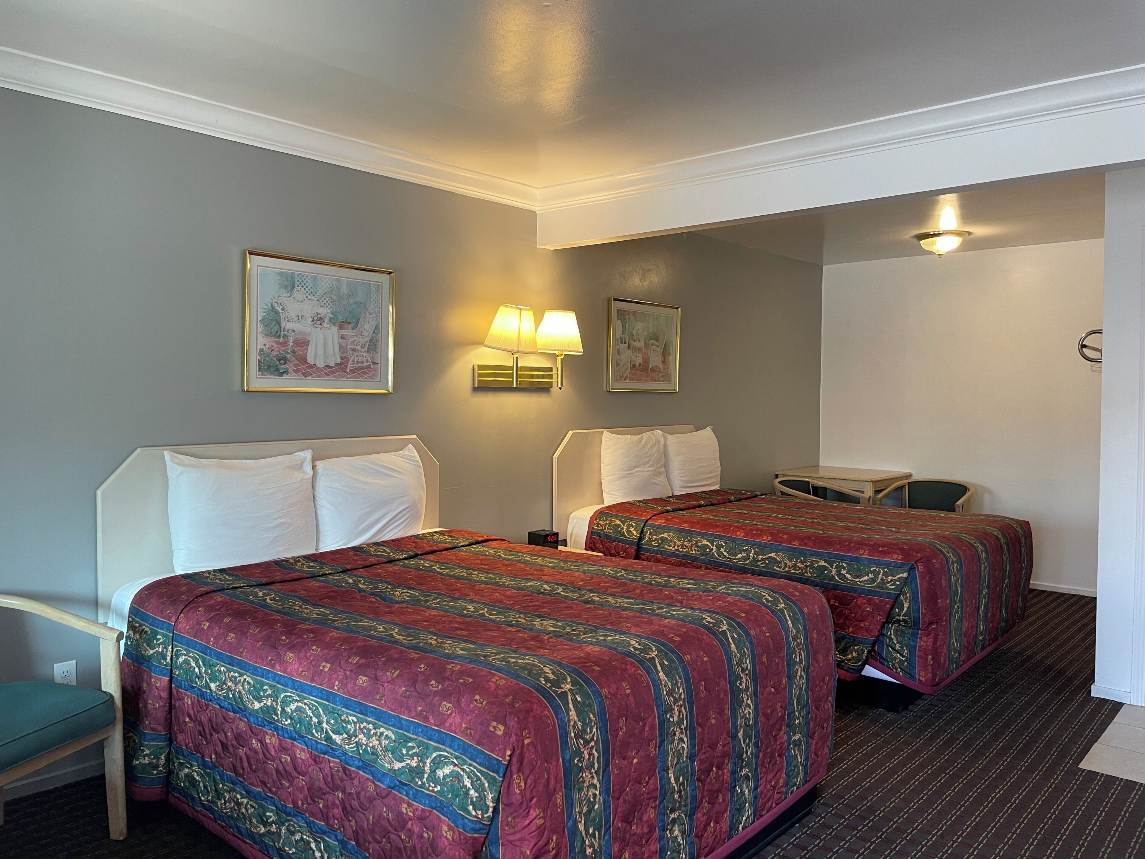 A hotel room with two beds, a desk, a chair, and two wall-mounted lamps.