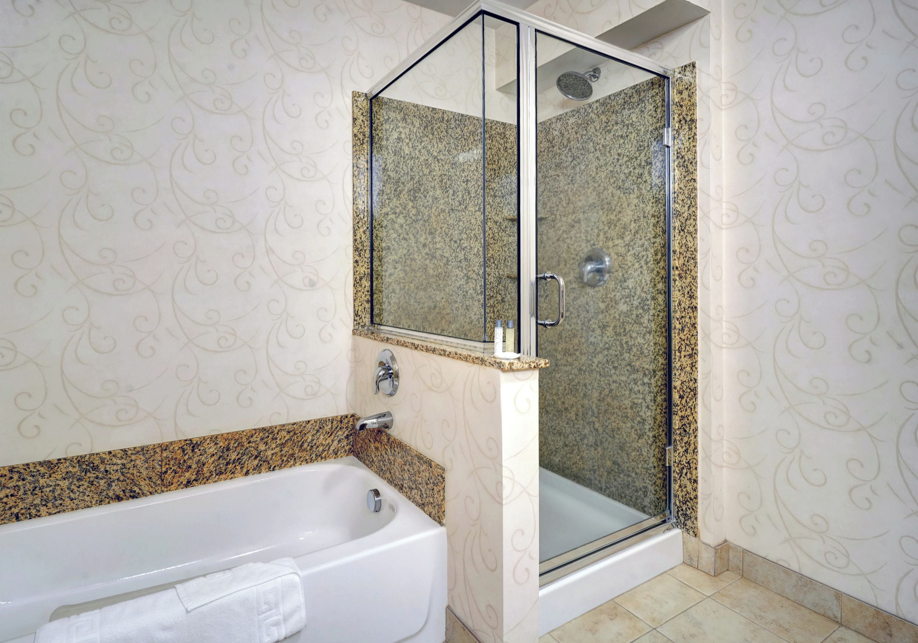 Une salle de bain dotée d’une douche à parois de verre, d’une baignoire blanche et d’un comptoir en granit.