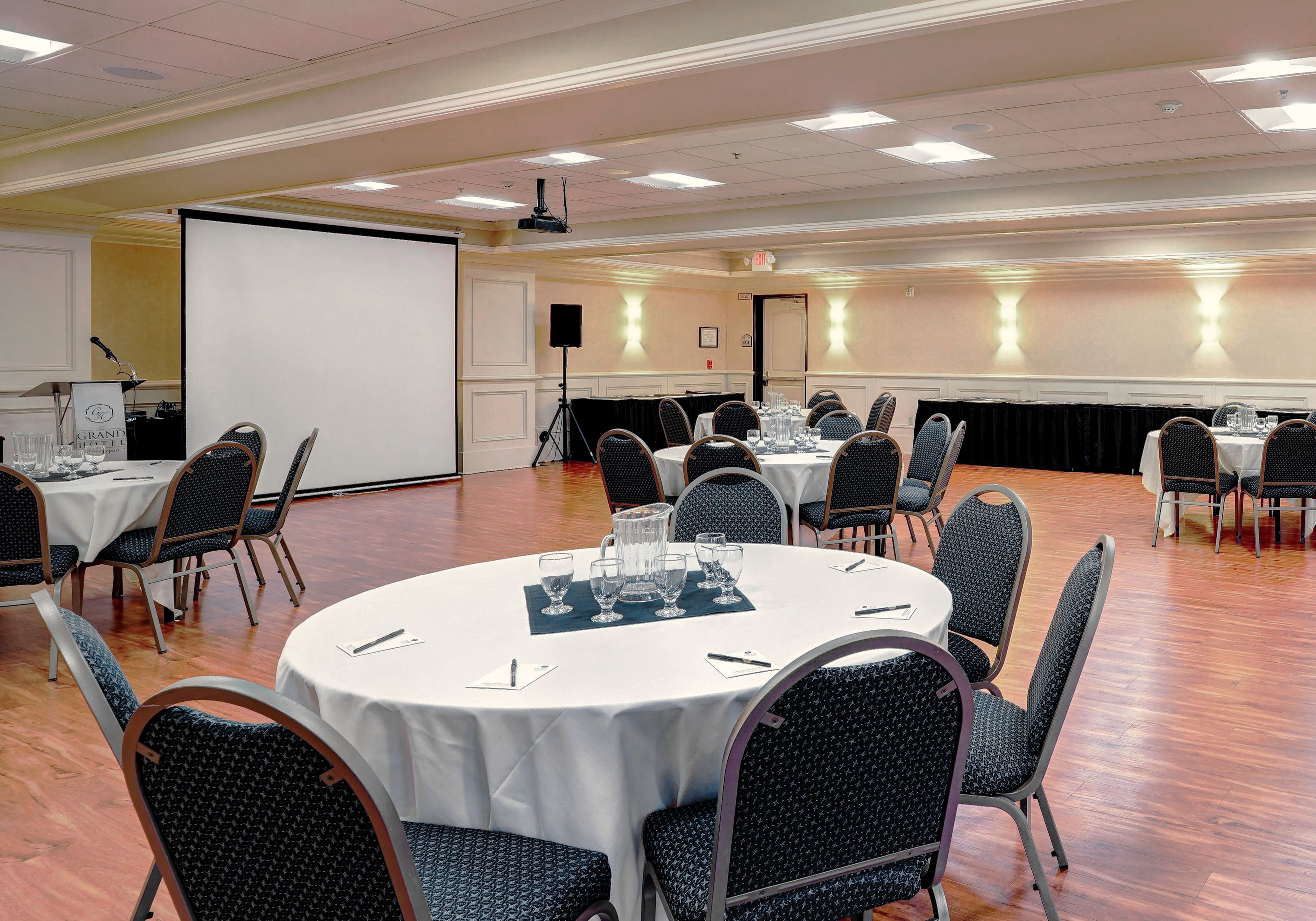 A conference room with round tables, chairs, a projector screen, and a speaker.