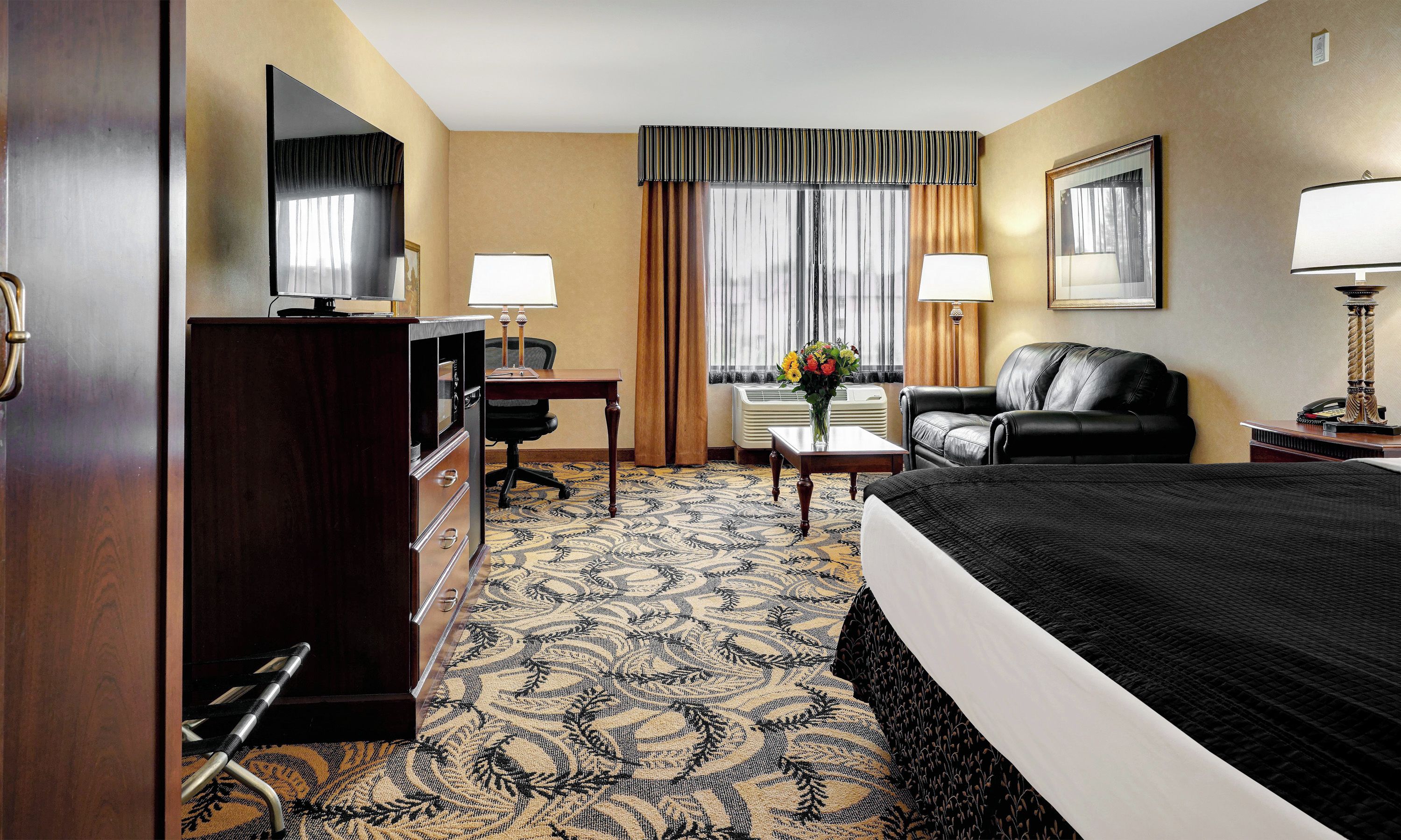 A hotel room with a bed, desk, chair, and a large mirror.