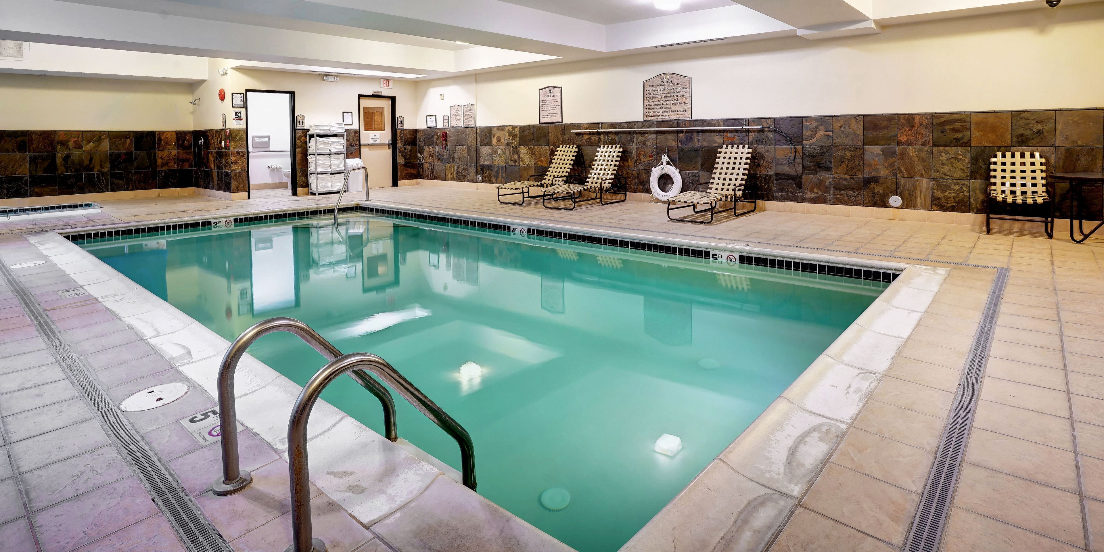 A swimming pool with a tiled deck, a lifeguard chair, and a towel rack.