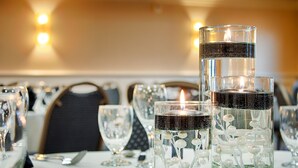 Une table dressée avec des chandeliers en verre transparent et une bougie allumée, entourée de verres à vin vides et de couverts.