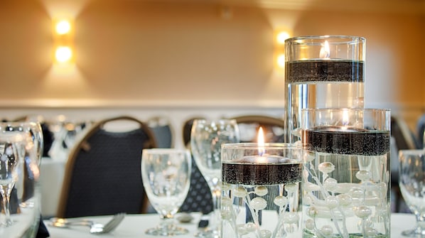 Une table dressée avec des chandeliers en verre transparent et une bougie allumée, entourée de verres à vin vides et de couverts.