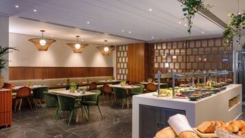 Un restaurante moderno con paneles de madera, sillas tapizadas de verde y una zona de bufé con pan y ensaladas.