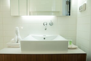 Un baño con un lavamanos blanco, un espejo encima y una toalla en la encimera.