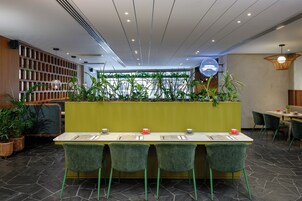 Un restaurante con una barra larga, sillas verdes y plantas en macetas.