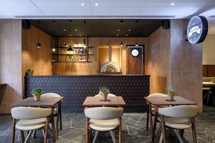 Interior de restaurante con mostrador, zona de mesas y horno para pizzas.